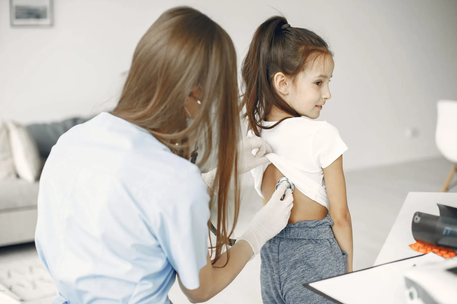 A clinician listens to a young girl's back with a stethoscope